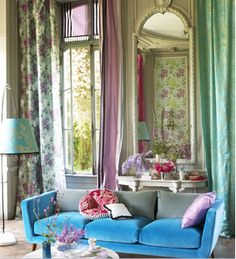 a blue couch sitting in front of a window next to a table with flowers on it