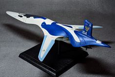 a blue and white model airplane sitting on top of a black stand with grey background