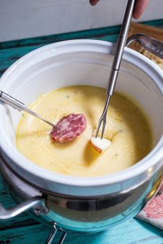 a person holding a spoon in a bowl with cheese and ham on the side, ready to eat