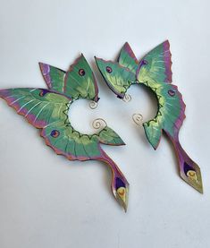 two green and purple leaf shaped brooches sitting on top of a white surface