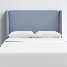 a bed with white pillows and blue headboard in a room that is painted light blue