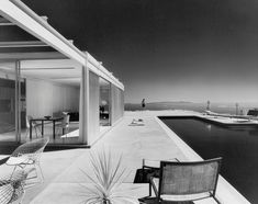 a black and white photo of some chairs on a patio next to the water with boats in the background