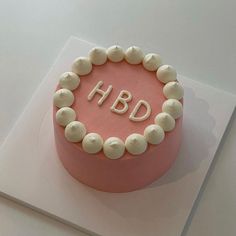 a pink cake with white frosting and the word hbd on it's side