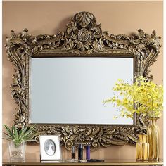 an ornate gold framed mirror sitting on top of a wooden table next to vases and flowers