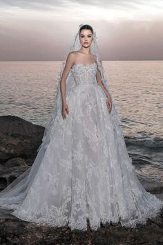 a woman in a wedding dress standing on rocks near the ocean with her veil over her head