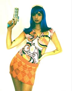 a woman with blue hair holding a cell phone in her right hand and wearing an orange skirt