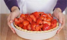 a person holding a pie with strawberries in it