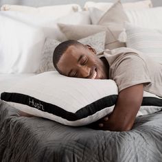 a man laying on top of a bed holding a pillow with the word hush written on it