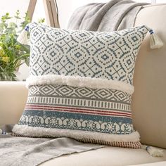 a white couch with a blue and red pillow on top of it next to a potted plant