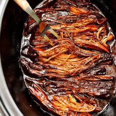 the meat is being cooked in the slow cooker with tongs and sauce on top