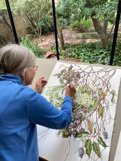 an older woman is painting in her backyard garden with plants and flowers on the canvas