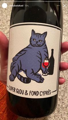 a person holding a bottle of wine with a cat on it's label in their hand