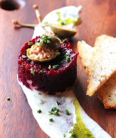 a wooden table topped with bread and jelly covered dessert next to an olive pickle