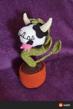 a knitted cow sitting on top of a purple blanket next to an orange object