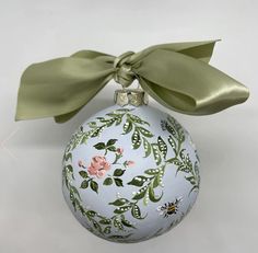 a white ornament with green leaves and flowers on it, tied with a bow