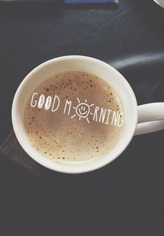 a cup of coffee with the words good morning written on it in white lettering, sitting on a black table