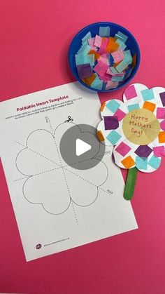 a paper flower next to a piece of construction paper and a blue bowl with scissors