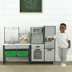 a young boy standing in front of a play kitchen with green drawers and white walls