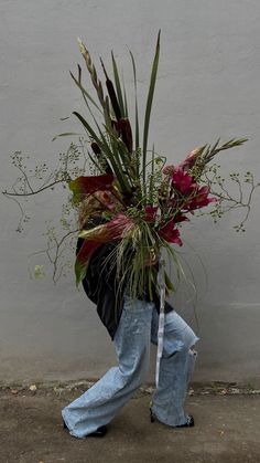 a person walking down the street carrying a bunch of flowers on their back and wearing jeans