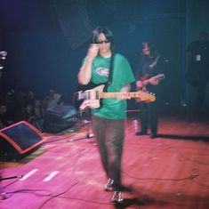 a man in green shirt holding a guitar and talking on cell phone while standing on stage