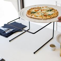 a person holding a plate with a pizza on it next to some condiments