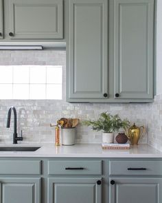 a kitchen with gray cabinets and white counter tops, plants on the sink area in front of the window