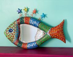 a colorful fish shaped mirror on top of a shelf next to starfishs and other decorations