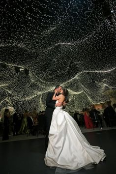 a bride and groom kissing in front of an array of lights