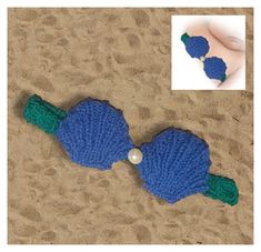 two crocheted blue and green fish with pearls on it's tail sitting in the sand