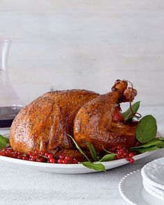 a roasted turkey on a plate with cranberries and leaves next to a glass of wine