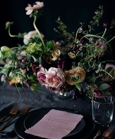 a black plate topped with flowers next to a glass filled with water and utensils