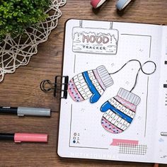 an open notebook with paper clips and markers on top of it, next to some pens