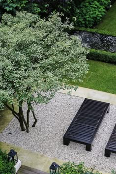 two black benches sitting on top of a gravel field next to a tree and shrubbery