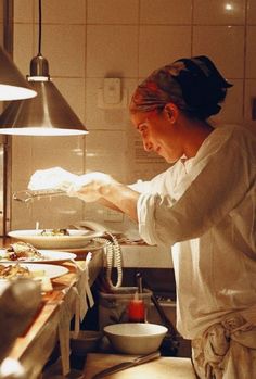 a woman in a kitchen preparing food on top of a counter next to a lamp