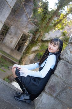 a young woman sitting on the side of a stone wall next to a brick building