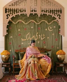 a woman sitting on top of a bed in front of a green wall with flowers