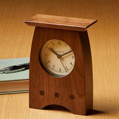 a wooden clock sitting on top of a table next to a pen and notebooks