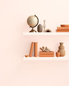 two white shelves with books and vases on them, against a pale pink wall