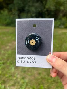 a hand holding up a black and yellow pin with the words homemade clay pins on it