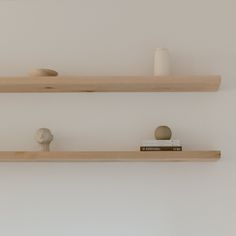 two wooden shelves with books and vases sitting on top of each other in front of a white wall