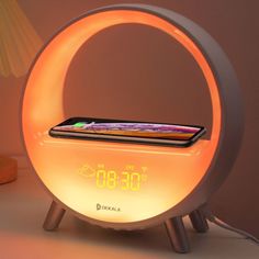 an alarm clock with a cell phone in it sitting on a table next to a lamp