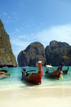 three boats are docked on the beach in front of some mountains and blue water with clear skies