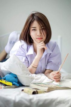 a woman laying on top of a bed holding a pencil