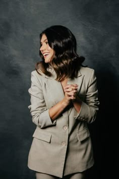 a woman standing in front of a black background wearing a suit and smiling at the camera