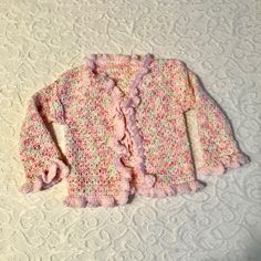 a pink sweater with ruffles on it sitting on a white tablecloth next to a pair of scissors