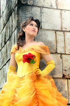 a woman in a yellow dress standing next to a brick wall with a rose on it