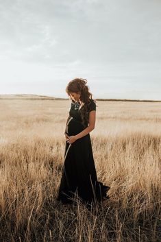 a pregnant woman in a black dress standing in a field