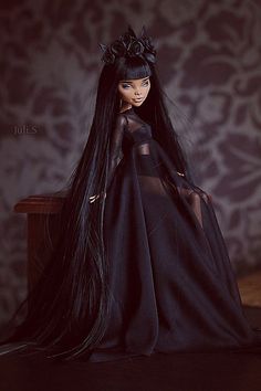 a doll with long black hair is sitting on a table and wearing a black dress