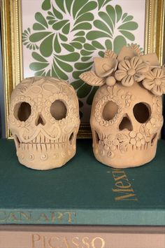 two ceramic skulls sitting next to each other on top of a green bookcase in front of a floral wallpaper