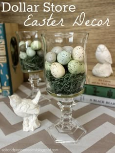 two glass vases filled with eggs and grass on top of a table next to books